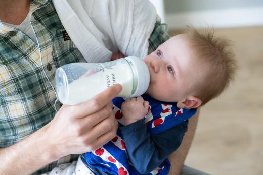 Wensvader geeft zijn zoon een flesmelk. De zoon ligt in de armen rustig zijn fles te drinken.