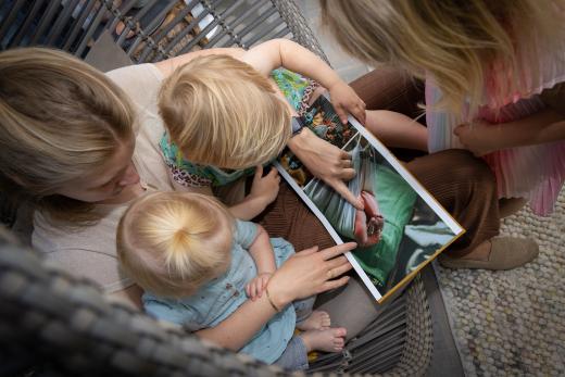 Draagmoeder zit met haar dochters en draagdochter een fotoboek te bekijken