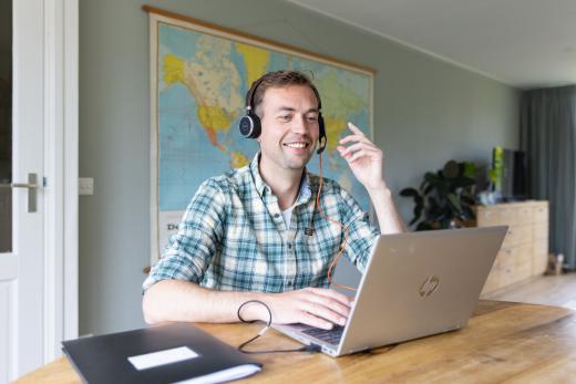 Man achter de computer met een koptelefoon op, kijkt en lacht naar de computerscherm.