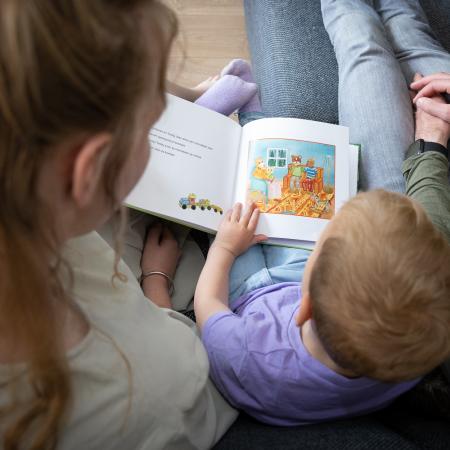 tussen een draagmoeder en vader zit een kind, ze lezen een boekje